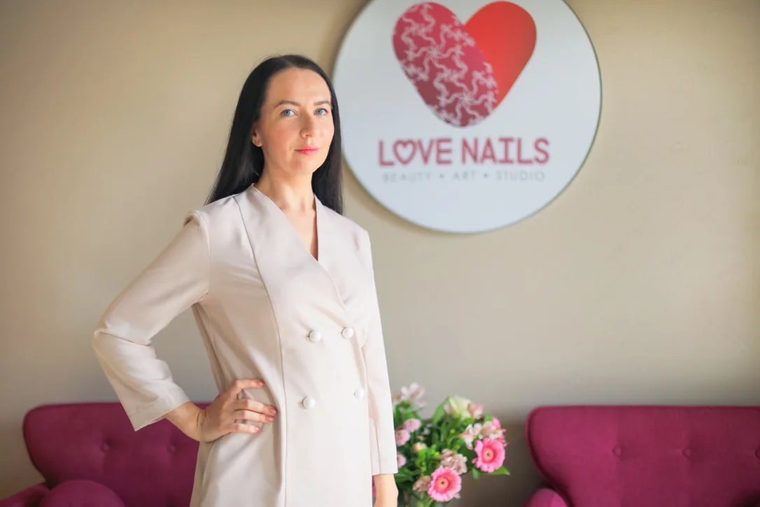 Marina in het LoveNails-salon in Geraardsbergen, voor het logo aan de muur
